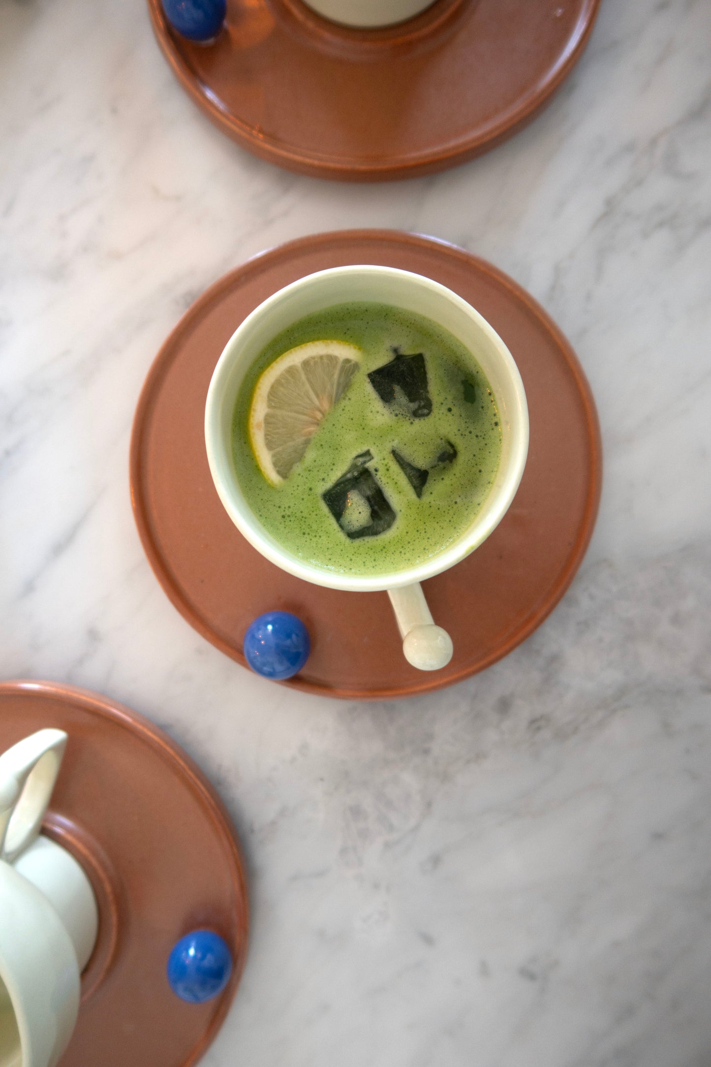 Cup of green tea with lemon slice and black tea bags on a brown saucer, marble background