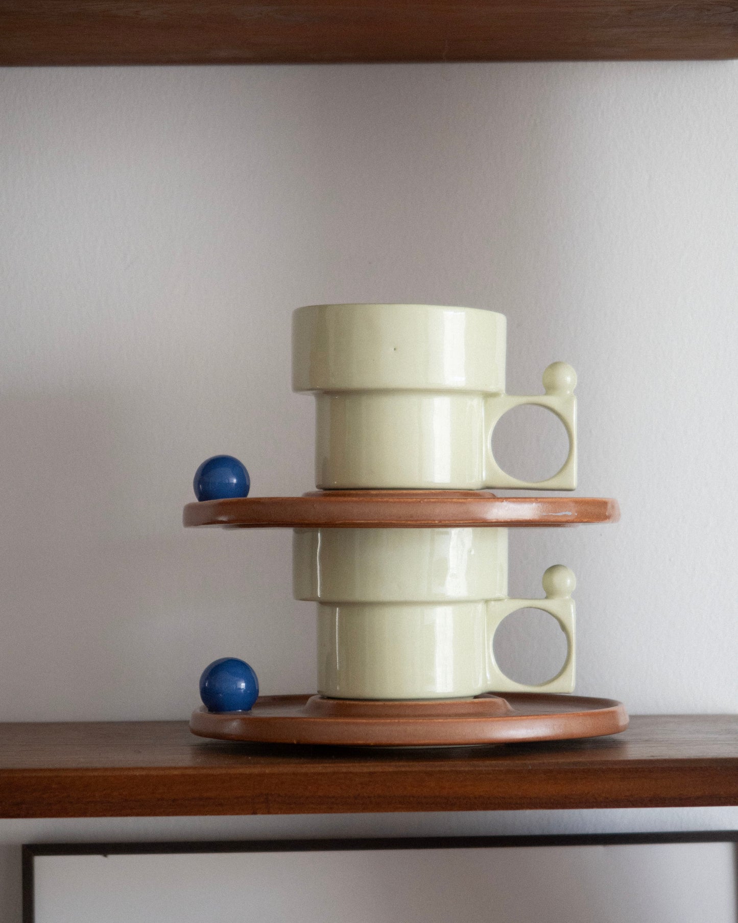 Decorative stack of cylindrical ceramic pieces on a wooden shelf with a plain background