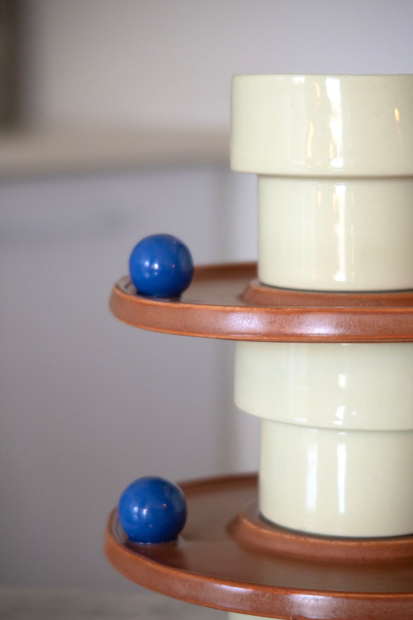 Decorative cylindrical object with a blue ball on a wooden shelf against a plain background
