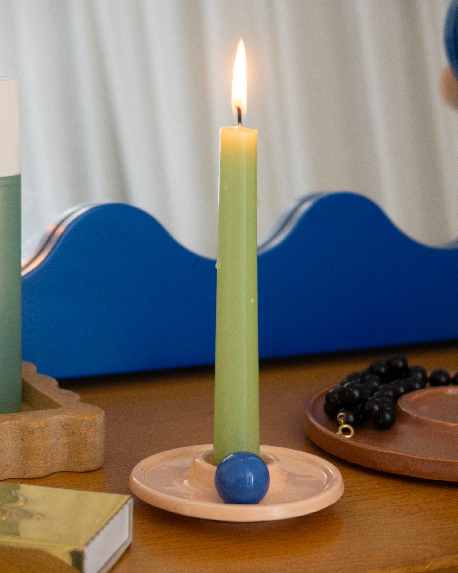 Green candle in a holder with a blue ball on a wooden surface, with a blurred background.