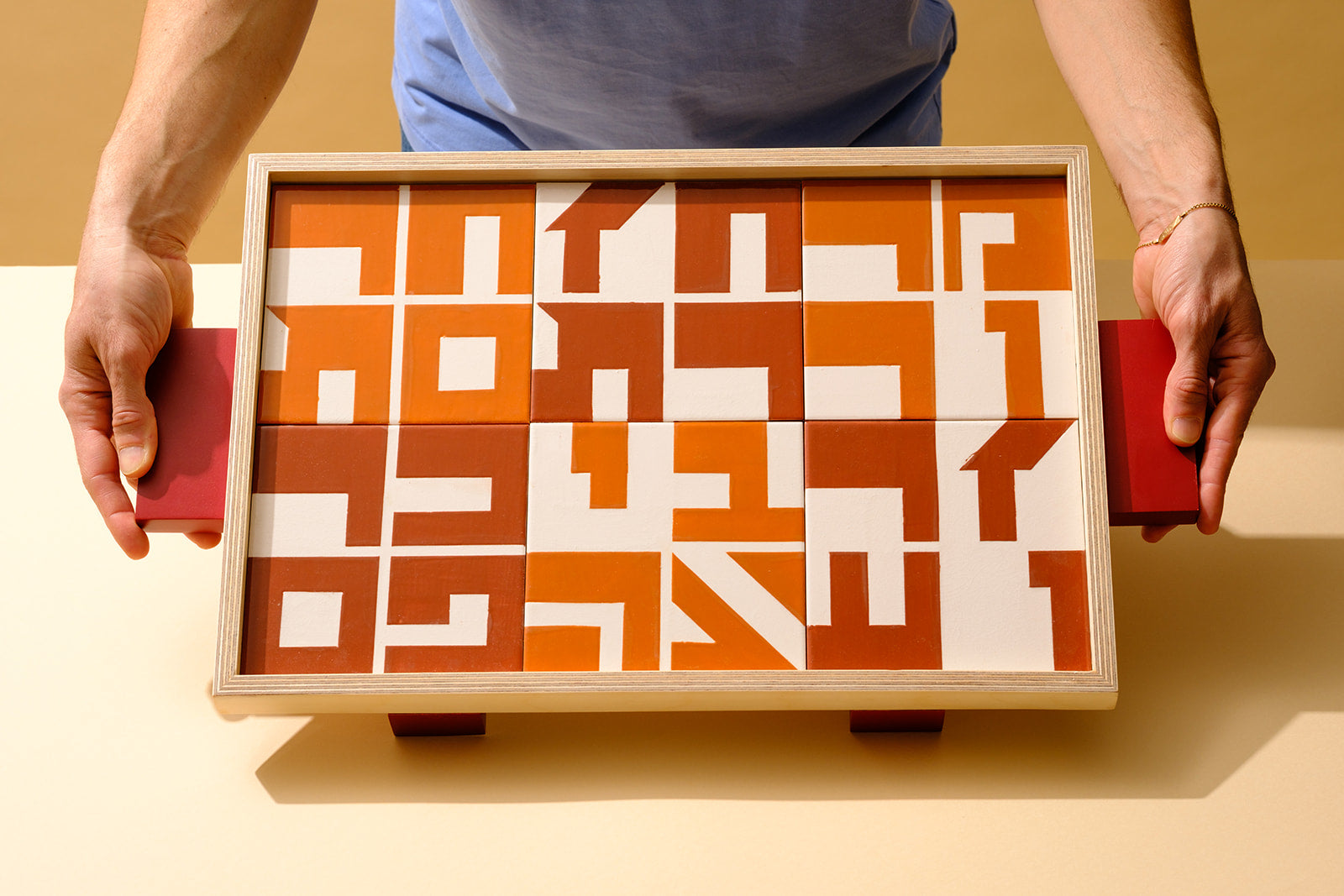 A wooden serving tray inlaid with hand-painted ceramic tiles, each featuring the name of a traditional Passover Seder food in Hebrew