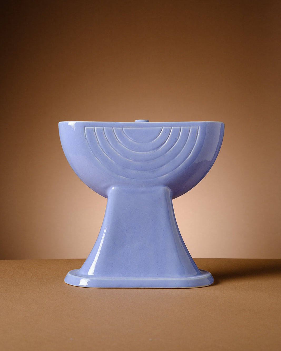 A sculptural lavender ceramic menorah by ABS Objects, handmade in Tel Aviv. The menorah features a semi-circular form with concentric geometric reliefs inspired by the logo of Israel’s first television channel. Its glossy surface and modernist silhouette reflect the studio's fusion of contemporary design, local history, and Hebrew visual culture. Photographed against a deep purple background, the piece embodies a modern take on Judaica with cultural and aesthetic depth.