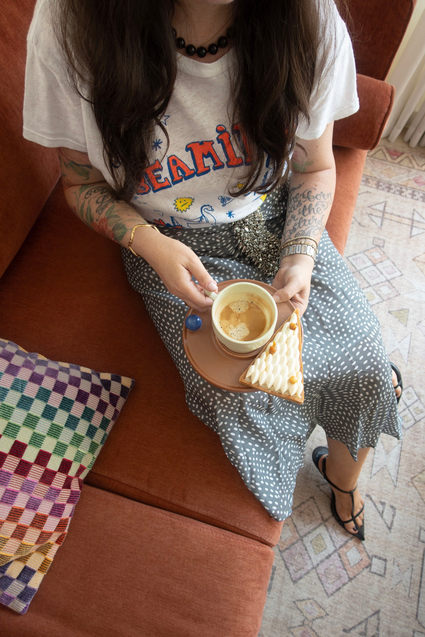 Person sitting on a couch holding a cup and a pastry