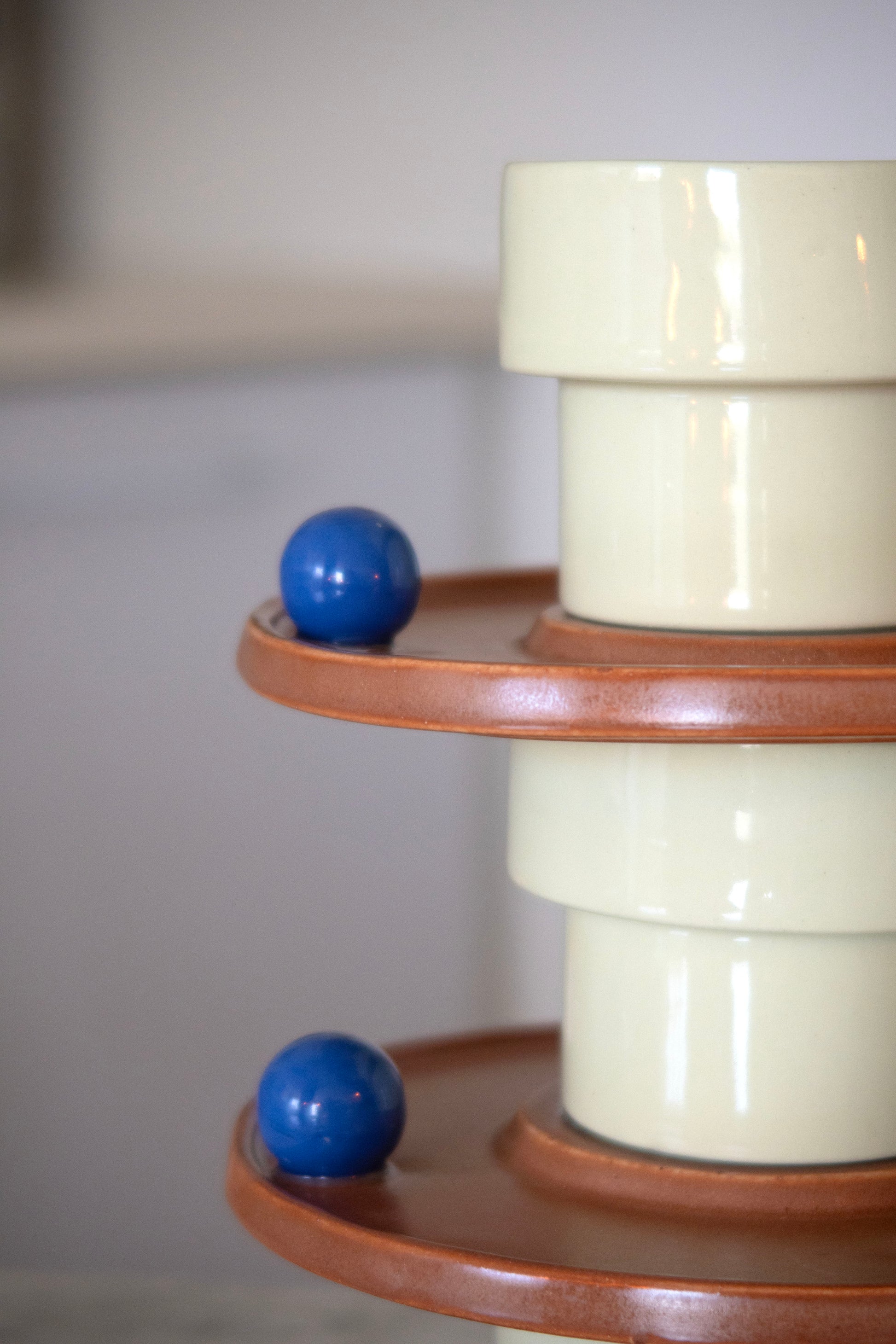 Decorative cylindrical object with a blue ball on a wooden shelf against a plain background
